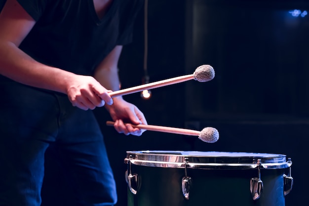 Il percussionista suona con le bacchette sul timpano in una stanza buia con una bella illuminazione. concerto e concetto di performance.