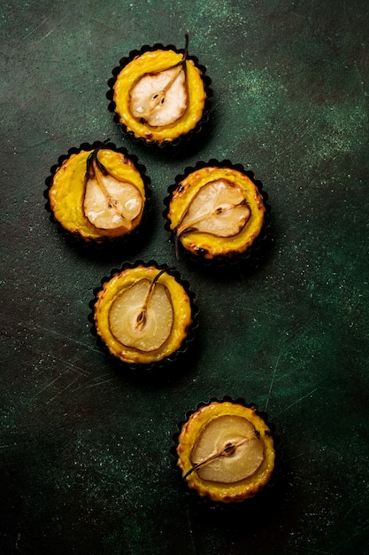 Peren en vla mini taartjes op een donkergroene betonnen oude tafel achtergrond.