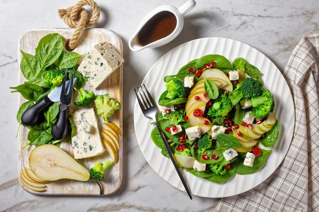 Perensalade met blauwe kaasblokjes, broccoli, spinazie, gedroogde cranberry en granaatappelzaden op een bord op een marmeren tafel, thanksgiving bijgerecht, horizontale weergave van bovenaf