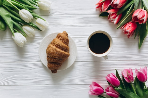 女性のための完璧な朝食。チューリップ、コーヒー、クロワッサンの花束。