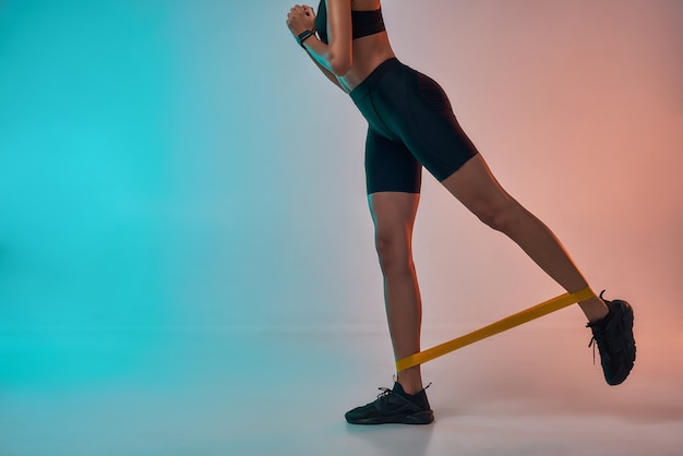 Perfect buttocks cropped photo of athlete woman in sports clothing exercising with a resistance band