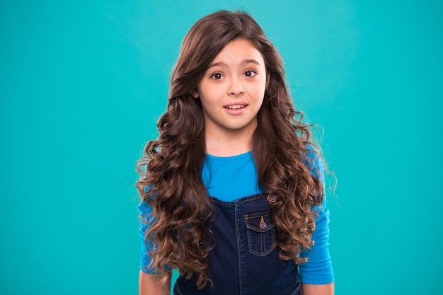 Perfect curling hair Teaching healthy hair care habits Kid girl long healthy shiny hair Kid happy cute face with adorable curly hairstyle stand over blue background Little girl grow long hair