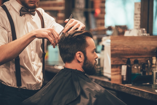 Taglio perfetto da dietro in avanti. primo piano di giovane uomo barbuto che ottiene taglio di capelli