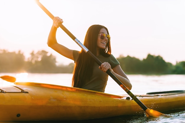 Perfect day for kayaking. Beautiful young smiling woman paddling while sitting in kayak
