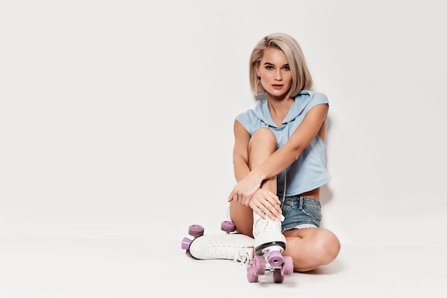 Perfect in every way. Attractive young woman in roller skates looking at camera while sitting against grey background