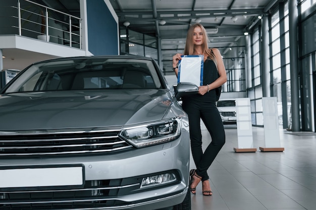 Perfect gepolijste auto. Meisje en moderne auto in de salon. Overdag binnen. Nieuw voertuig kopen.