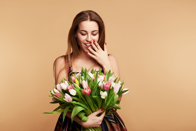 Perfect gift. Wonderful flowers on Womens Day. Tender smiling brunet woman poses with colorful tulips, looks happily. Space for text