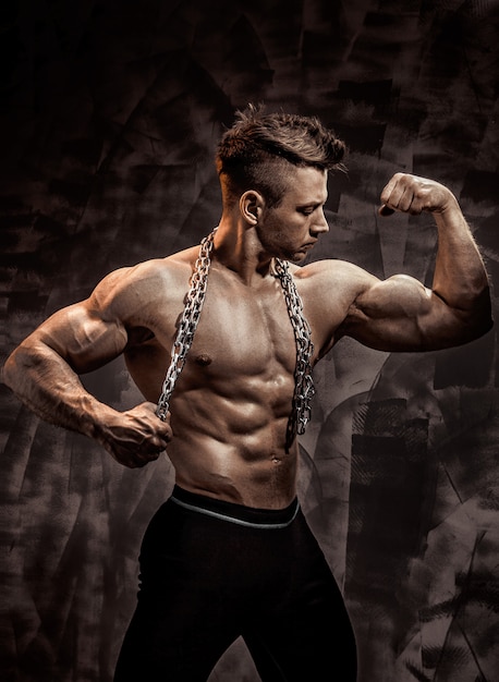 Photo the perfect male body - awesome bodybuilder posing. hold a chain with tattoo
