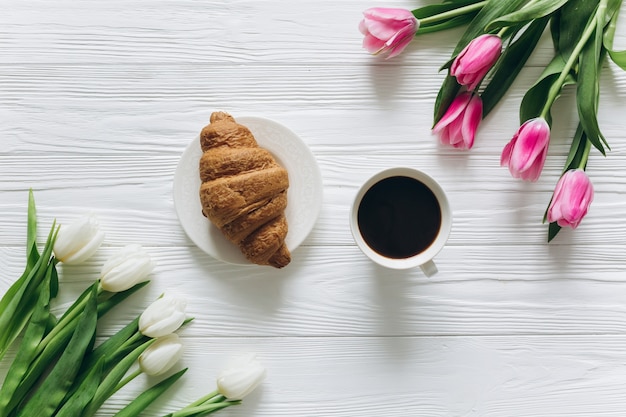 Perfect ontbijt voor vrouwen. Boeket tulpen, koffie en een croissant.