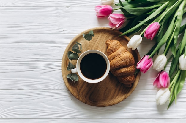 Perfect ontbijt voor vrouwen. Boeket tulpen, koffie en een croissant.