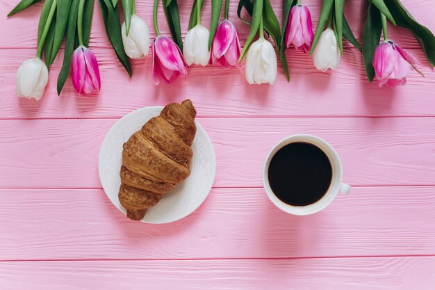 Perfect ontbijt voor vrouwen. Boeket tulpen, koffie en een croissant.