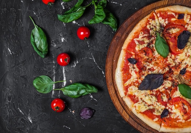 Perfect pizza margarita with tomato slices basil and cherry tomatoes on a dark surface