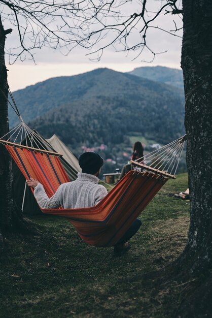 Perfect place to stay. Rear view of young man sitting in hammock while camping with his girlfriend