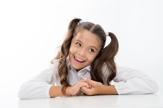 Perfect schoolgirl with tidy fancy hair. School hairstyle ultimate top list. Prepare kid first school day. Schoolgirl happy carefree face cute ponytail. Excellent pupil lean on desk isolated white.