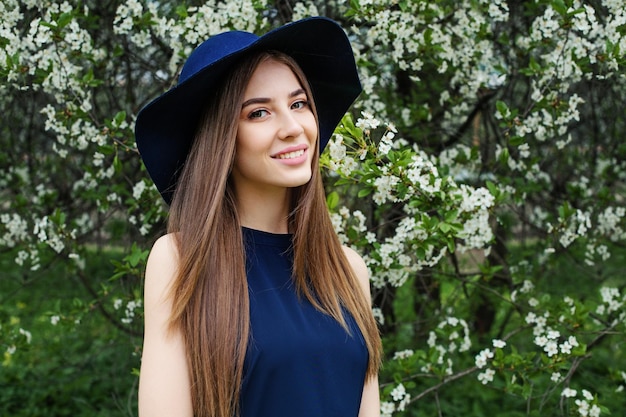 Perfect spring woman in blue hat outdoors Smiling girl against flowers background