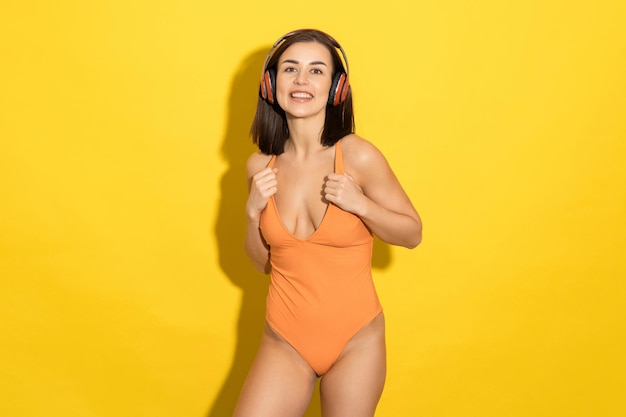 The perfect summer day is depicted in this image of a young woman enjoying her music in a swimsuit against a sunny yellow background
