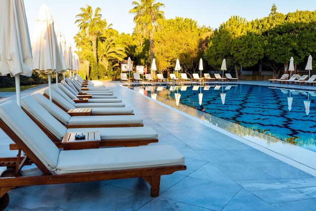 Perfect summer day at a luxury resort with deck chairs and parasols waiting by a crystalclear pool surrounded by lush greenery