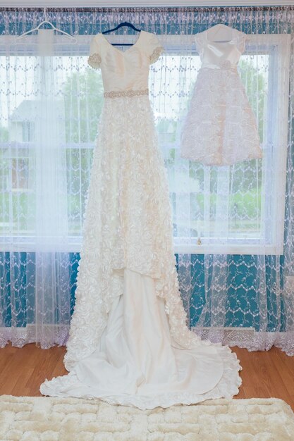 The perfect wedding dress with a full skirt on a hanger in the room of the bride with blue curtains