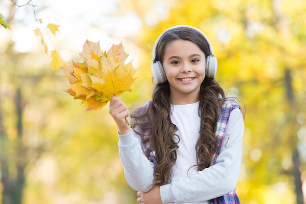 Perfecte herfstdag van een vrolijk kind, luister naar een audioboek of muziek met een koptelefoon in het herfstseizoen parkspel met gele gevallen esdoornbladeren onderwijs