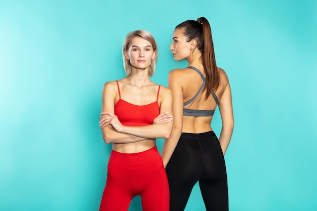 Perfectie twee mooie sportieve meisjes in sportkleding poseren in de studio tegen een blauwe achtergrond
