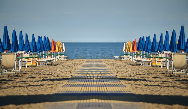 Vista perfettamente speculare e simmetrica della spiaggia con ombrelloni e lettini di lignano sabbia d'oro in italia. uno scenario privo di persone che regalano emozioni di calma e pace come solo il mare sa fare.