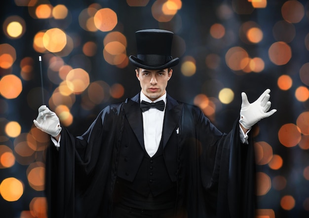 사진 공연, 서커스, 쇼 개념 - 모자를 쓴 마술사와 가까운 조명 배경 위에 마술 지팡이로 트릭을 보여주는 마술사