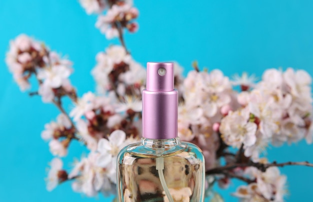 Perfume bottle and Beautiful flowering branches on blue background