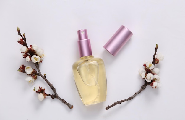 Perfume bottle and beautiful white flowering branches on white background Springtime beauty concept Flat lay top view