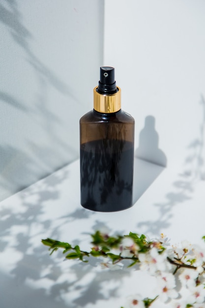 Perfume bottle and cherry branch with flowers in a white corner