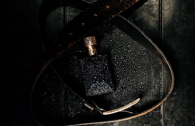 香水瓶、ダークメタリックの背景に革ベルト。クローズアップ、男性のアクセサリー。