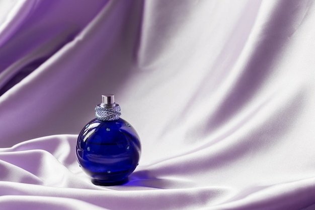 Perfume bottle on lilac silk folded fabric. Luxury Scent fragrance cosmetic beauty product.