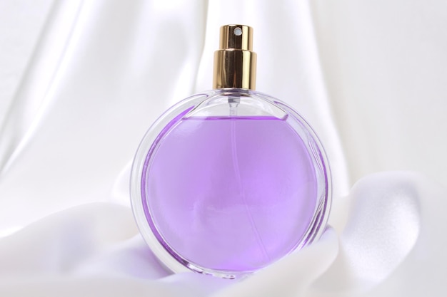 シルクの折り畳まれた生地の背景のパッケージデザインの香水瓶は、香りの香りの化粧品の美容製品をモックアップします