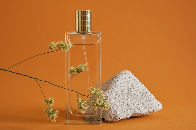 Perfume bottle, stone and blade of grass on brown background