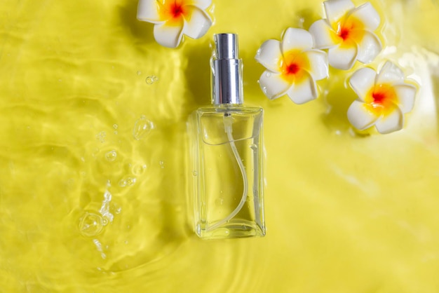 perfume bottle in water with drops with palm leaf and mango flowers on yellow background