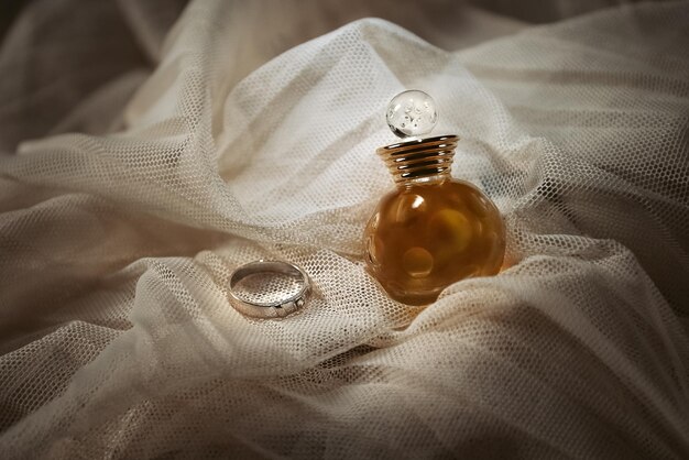 Perfume bottle and wedding ring on draped textile background