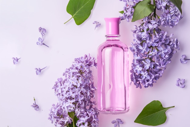 Perfume bottle with lilac flowers on white wall