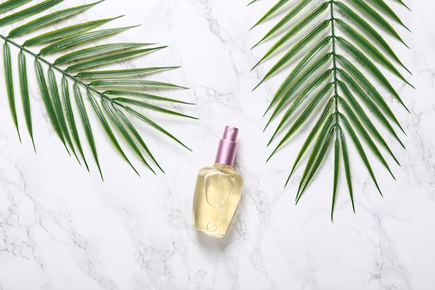 Perfume bottle with palm leaves on marble background