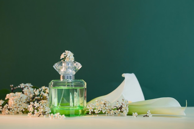 Perfume bottle with plants and flowers on green background