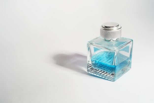 Духи в прозрачной бутылке светло-голубого цвета на белом фонеАроматерапия производство парфюмерии Место для текста