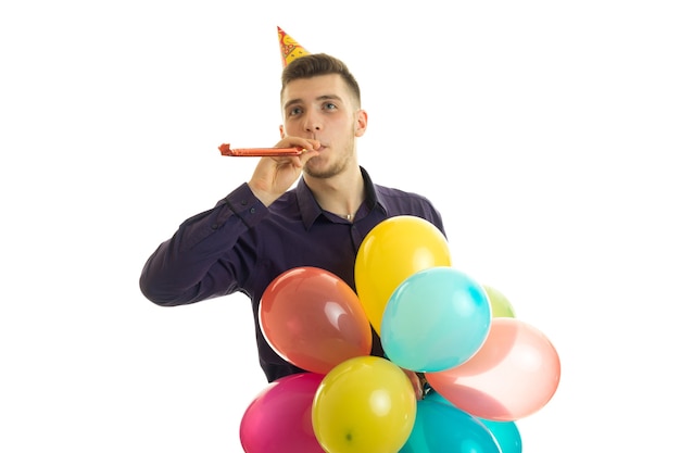 Perky young guy with a cone on his head keeps near dudelku mouth and many colored hot air balloon isolated on white background