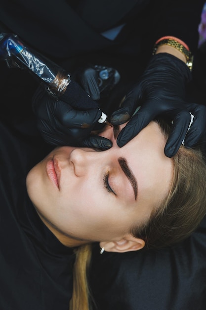 Photo permanent makeup beauty procedures the master applies a tattoo on the eyebrows professional facial microblading women's cosmetology device