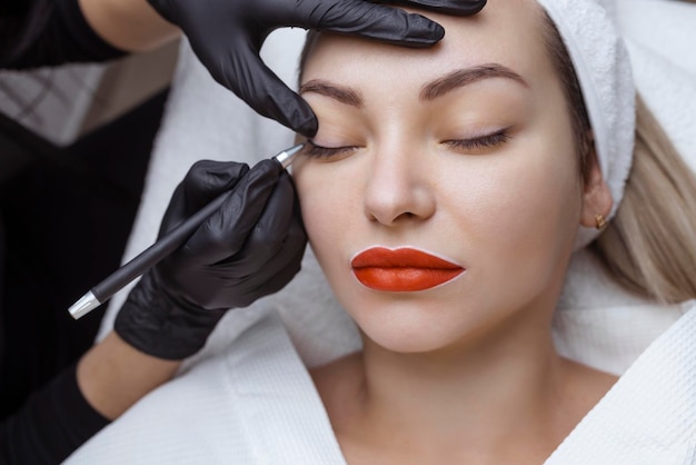 Permanent makeup Cosmetologist tattoo artist applies a contour to the client39s eyelid for subsequent application of eye tattooing