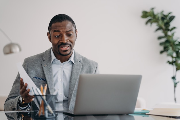 Uomo d'affari afroamericano perplesso guardando lo schermo del laptop che legge le cattive notizie nell'e-mail alla scrivania