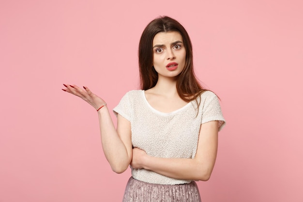 Perplexed concerned young woman in casual light clothes posing isolated on pastel pink wall background studio portrait. People sincere emotions lifestyle concept. Mock up copy space. Spreading hands.