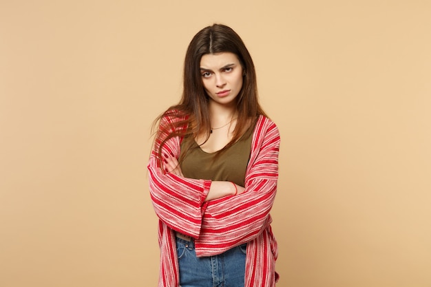 Perplexed puzzled young woman in casual clothes looking camera holding hands crossed isolated on pastel beige wall background in studio. People sincere emotions, lifestyle concept. Mock up copy space.