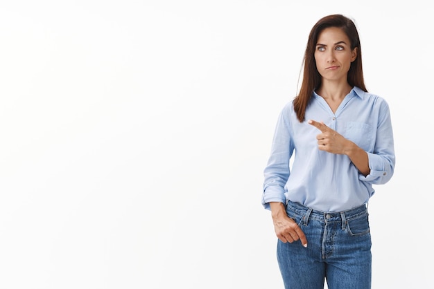 Perplexed thoughtful adult female entrepreneur deep thought making important decision smirk hesitant look pointing left doubtful focus task observe coworker project stand white background