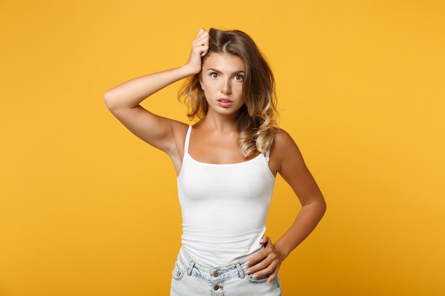 Perplexed young woman girl in light casual clothes posing isolated on yellow orange background, studio portrait . People sincere emotions lifestyle concept. Mock up copy space. Putting hand on head.