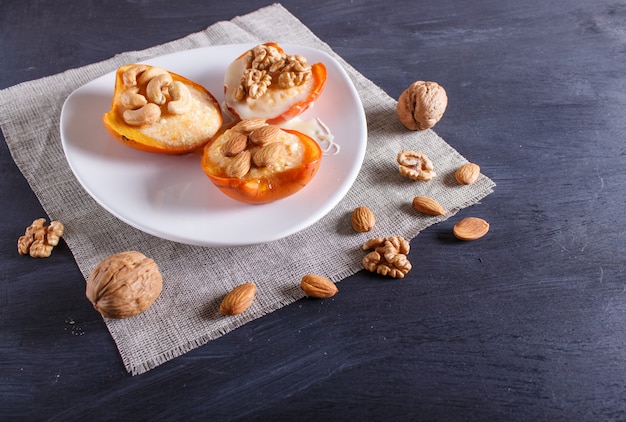 Persimmon dessert with curd, nuts and milk cream on black wooden surface.