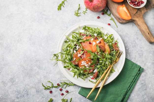 Persimmon salad with arugula, nuts, goat cheese, pomegranate. Healthy vegetarian food concept.