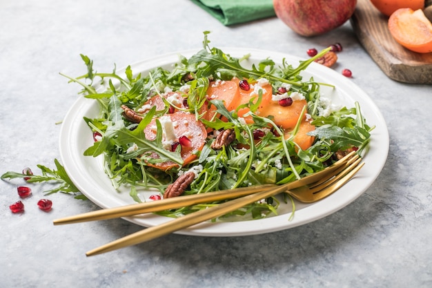 arugula, 견과류, 염소 치즈, 석류를 곁들인 감 샐러드. 건강한 채식 음식 샐러드 개념입니다.